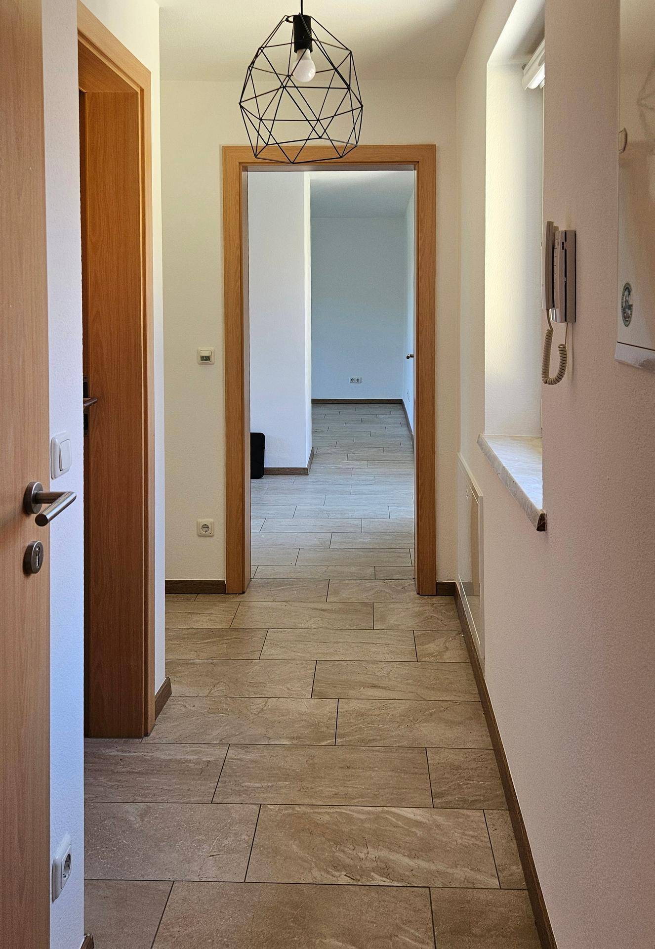 Heller Flur mit Fliesenboden, Holztüren und Blick in angrenzende Räume.