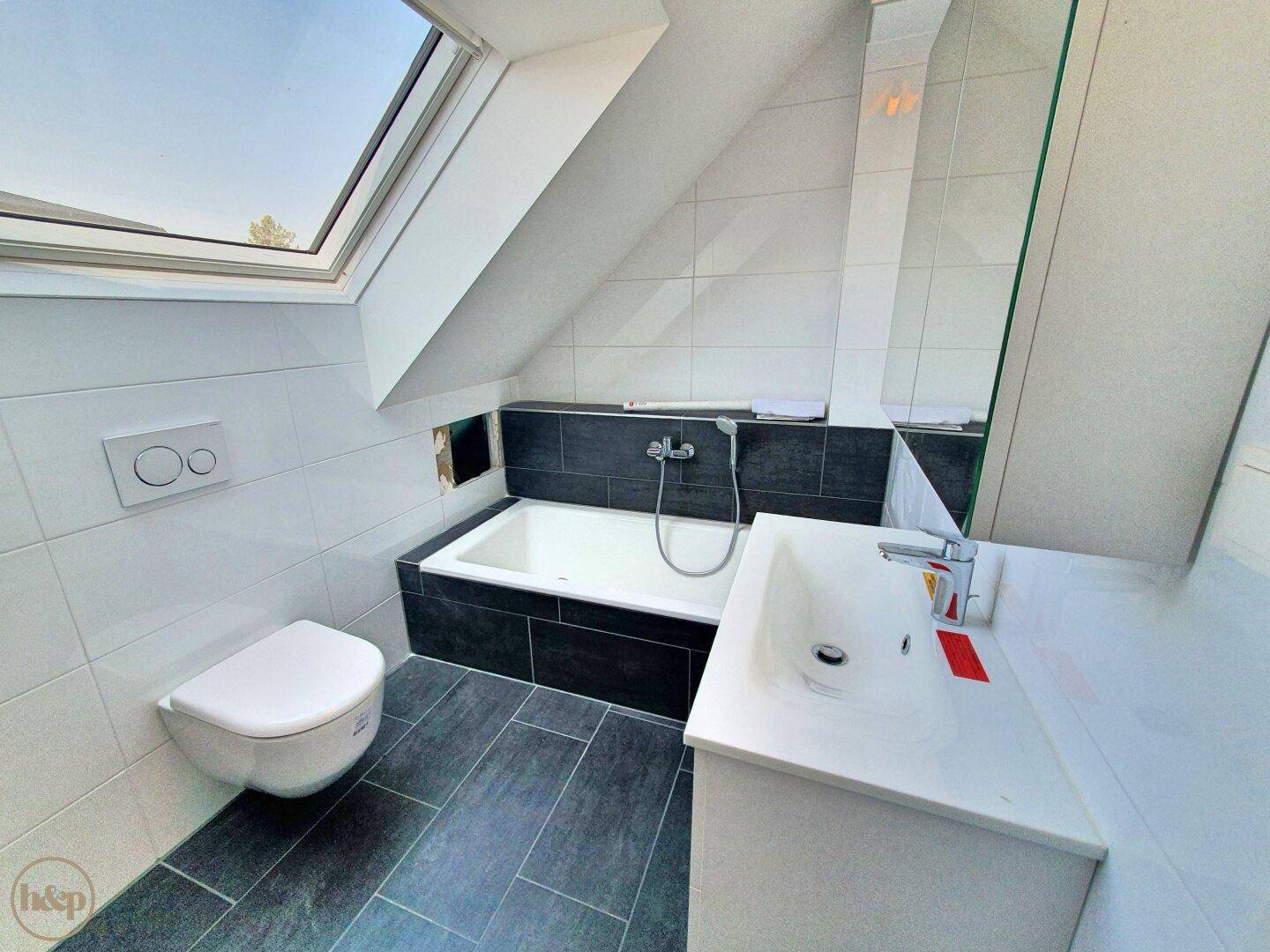 Modernes Badezimmer im Dachgeschoss mit Badewanne, WC, Waschbecken und Dachfenster.