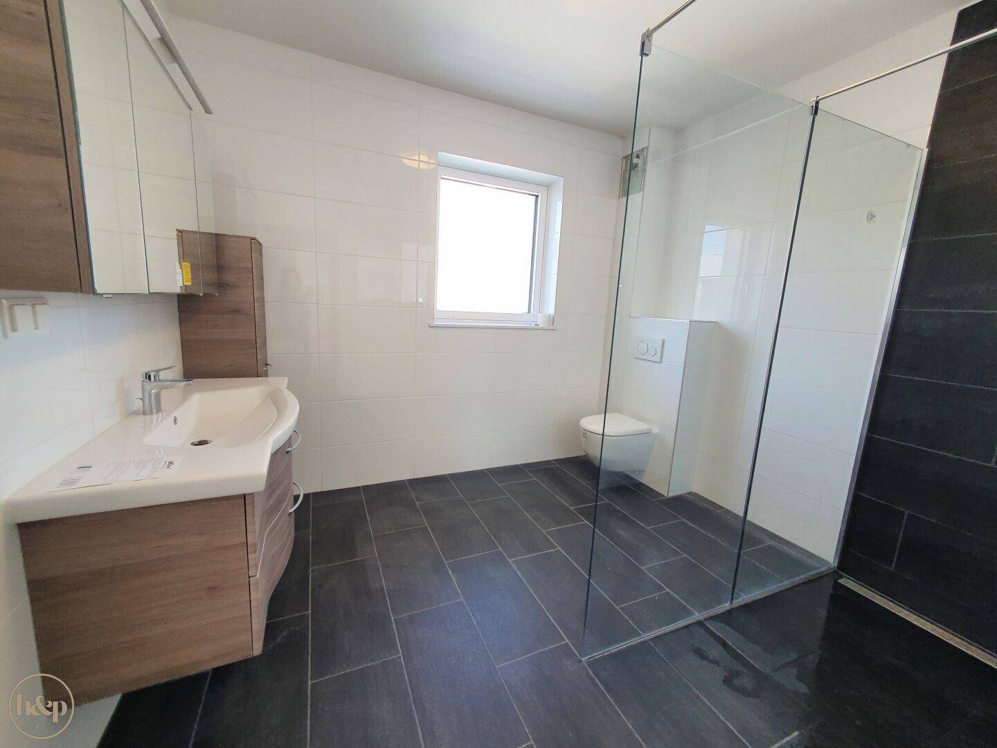 Helles Badezimmer mit moderner Dusche, Fenster und elegantem Waschtischunterschrank.