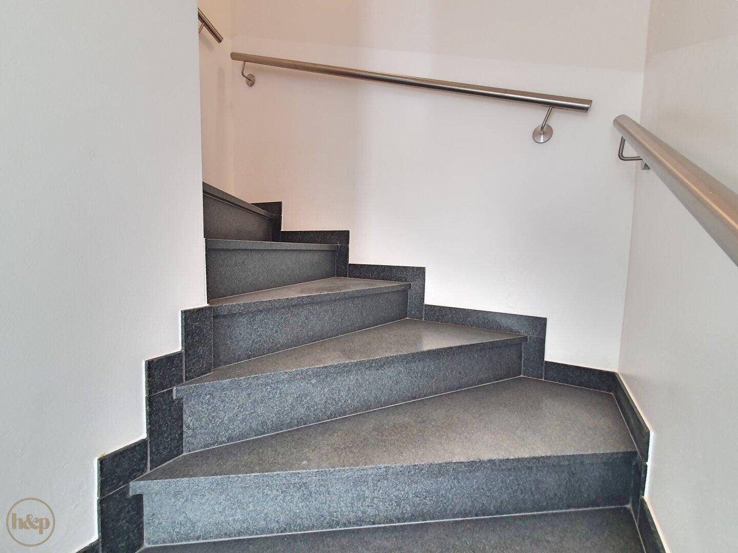Treppenhaus mit eleganten Steinstufen und modernem Edelstahlgeländer.