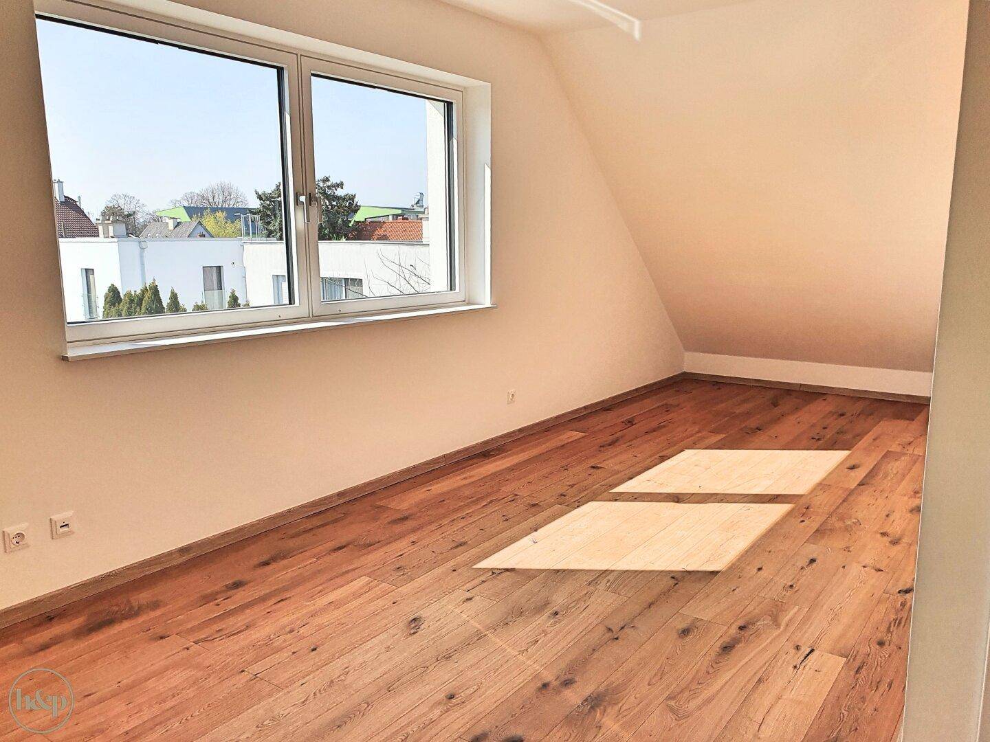 Helles Dachgeschosszimmer mit Holzboden, großem Fenster und schräger Decke.