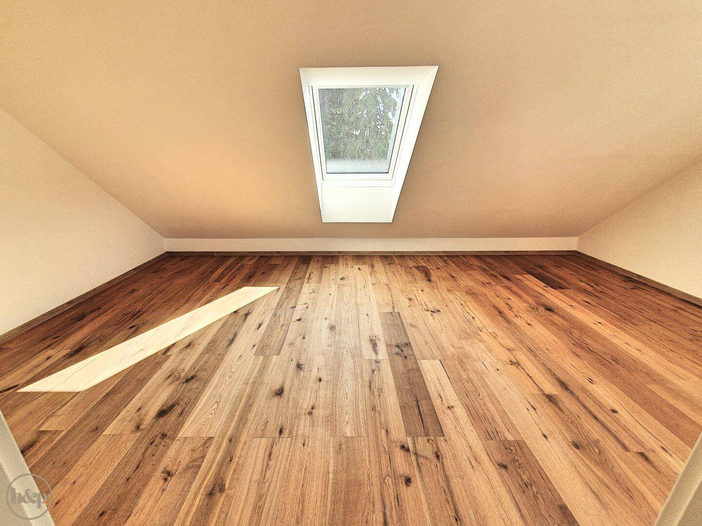 Dachgeschossraum mit Holzboden und Dachfenster, das viel Tageslicht hereinlässt.