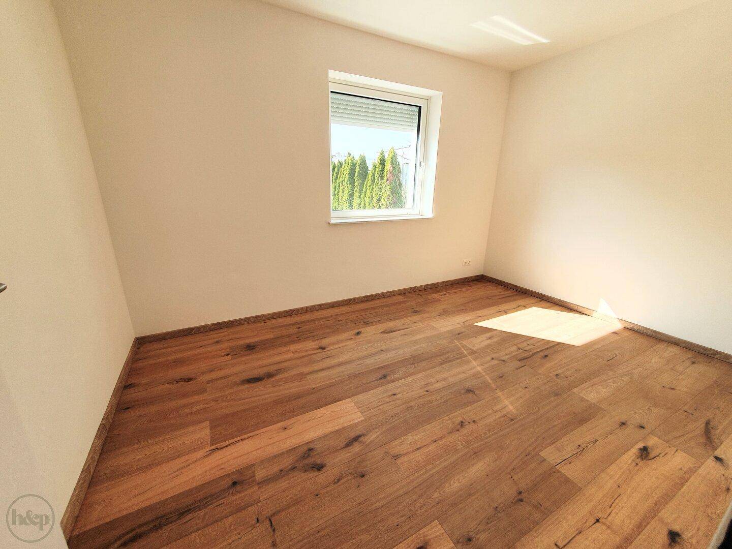 Helles Schlafzimmer mit Holzboden und Fenster, das einen Blick ins Grüne bietet.