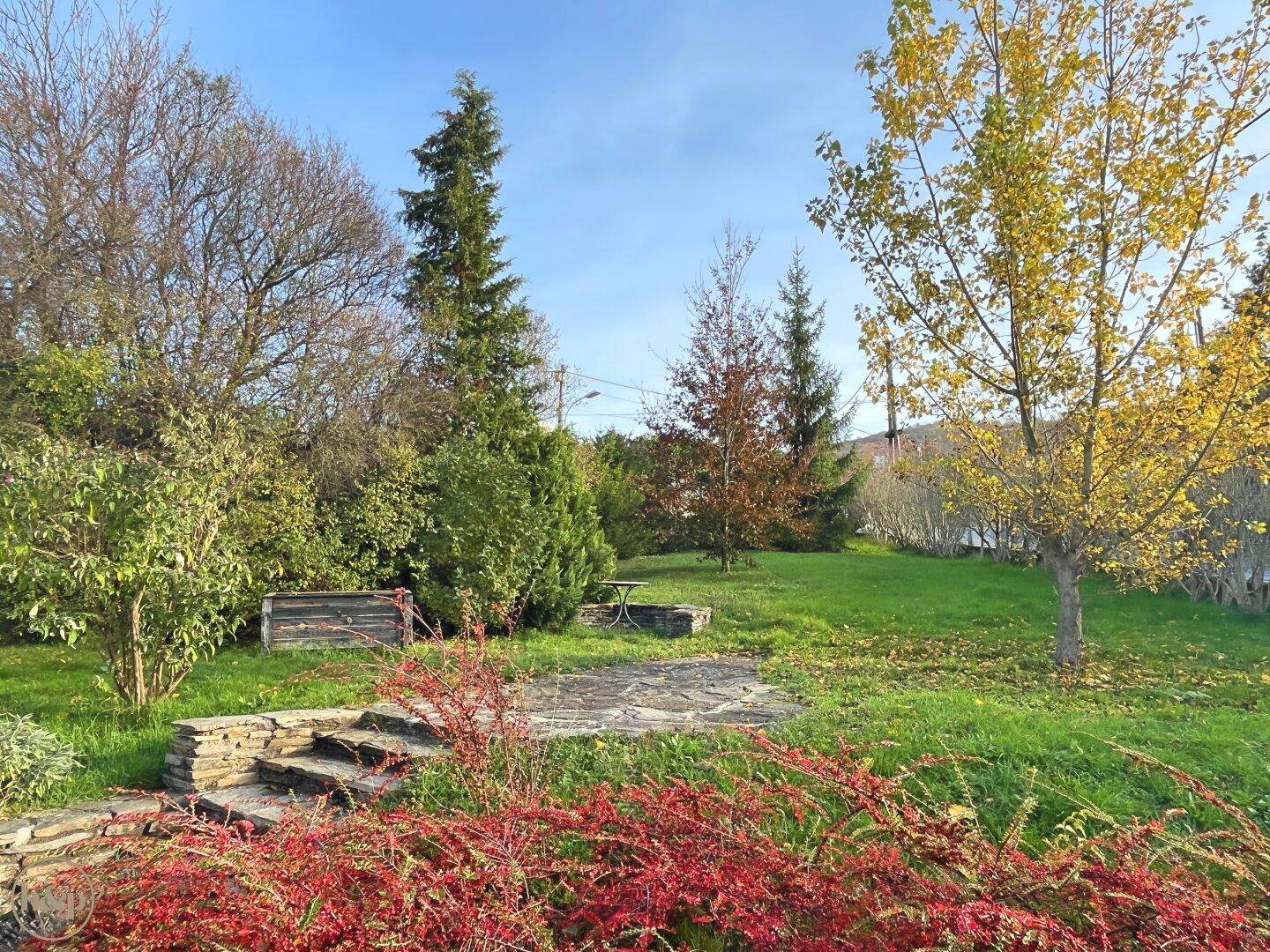 Garten mit Steinterrasse, Treppe und einem kleinen Tisch, umgeben von Grünflächen.