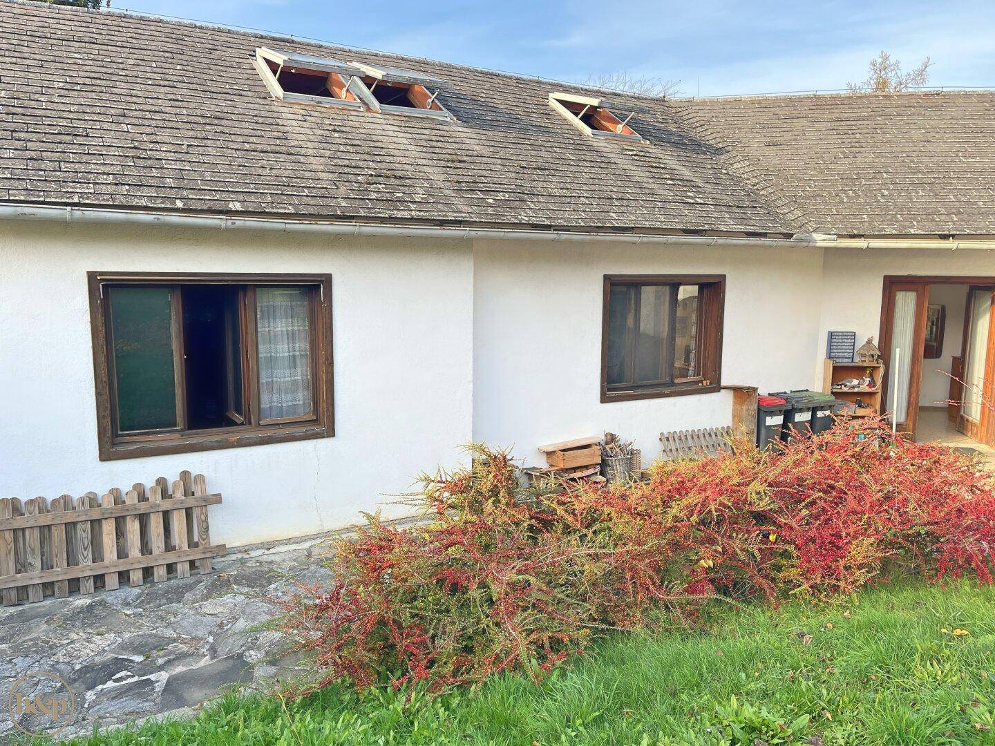 Rückseite eines Hauses mit Fenstern, einer Tür und einem Dach mit Dachfenstern.
