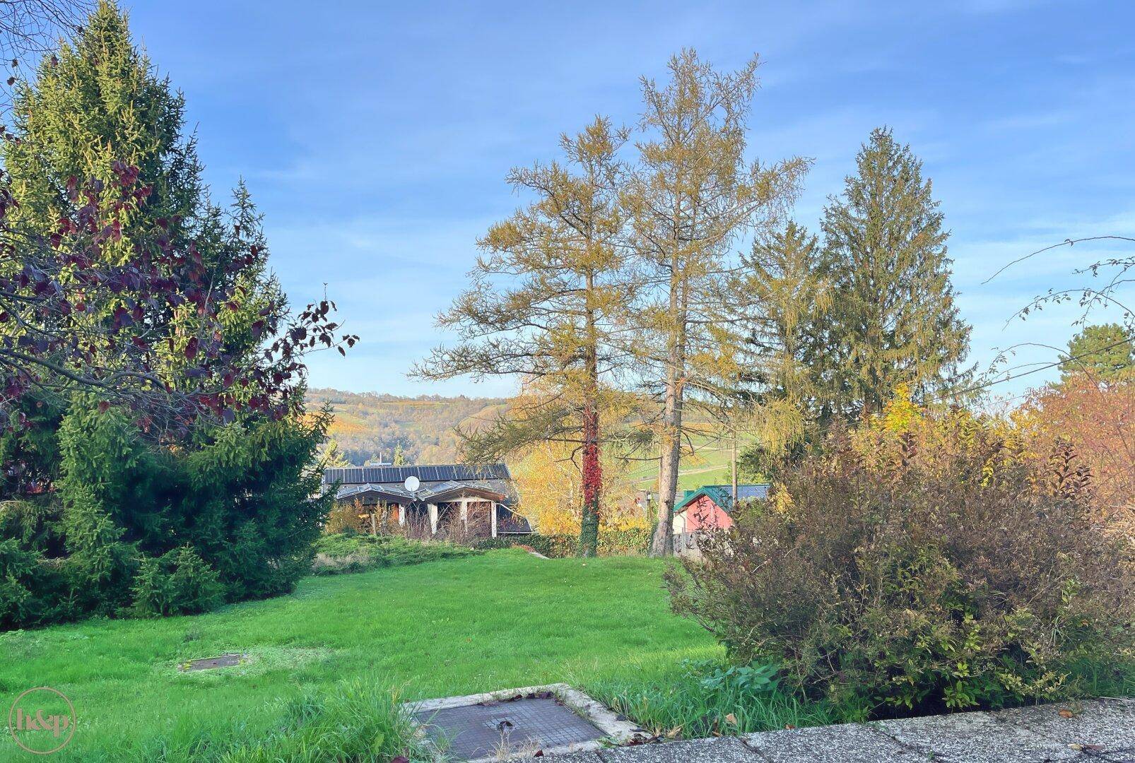 Garten mit Rasenfläche, Blick auf ein Haus mit Solaranlage und die herbstliche Landschaft.