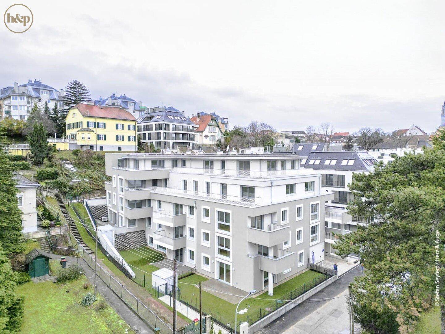 Moderne Wohnanlage mit mehreren Etagen und begrünten Außenbereichen in hügeliger Umgebung.