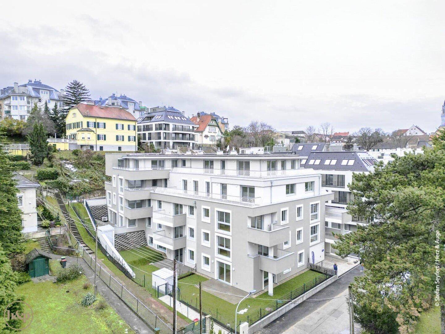Moderne Wohnanlage mit mehreren Etagen und umliegenden Grünflächen in hügeliger Umgebung.