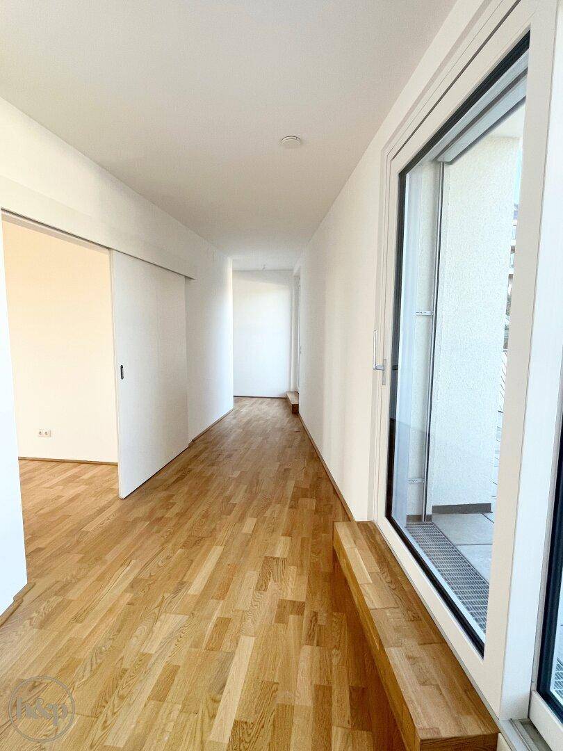 Heller Flur mit Holzboden und Schiebetüren, der zu weiteren Räumen führt.