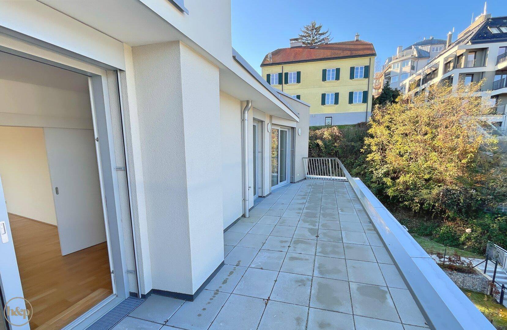 Große, geflieste Terrasse mit weißem Geländer und Blick auf die umliegende Bebauung.