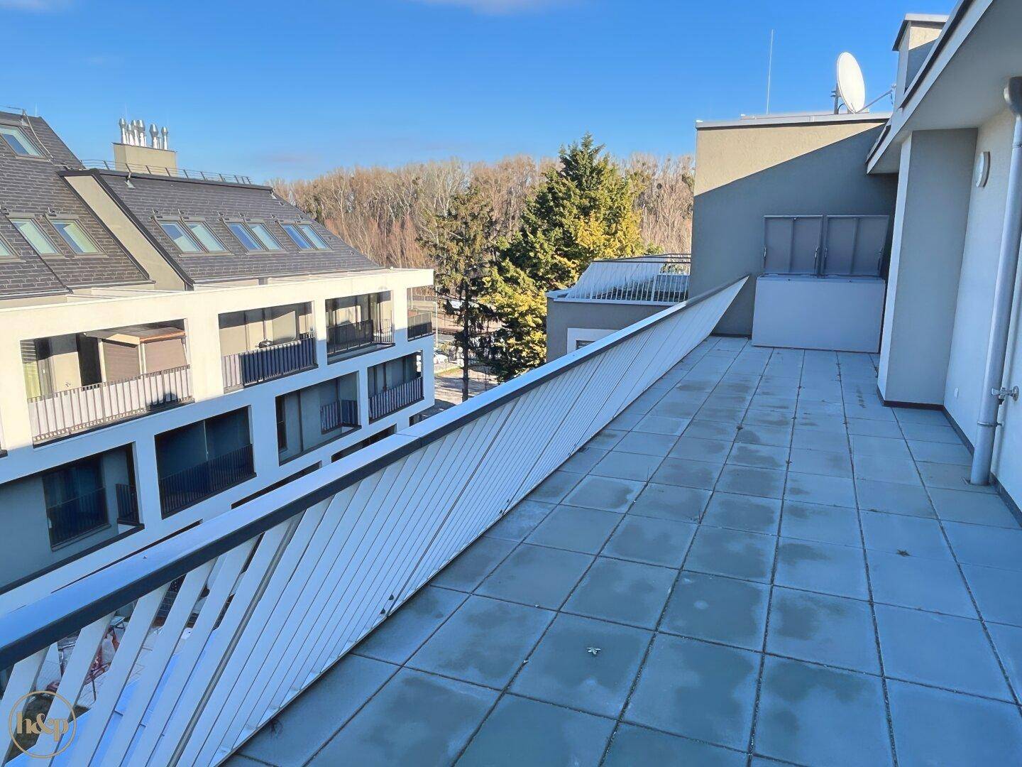 Weitläufige Terrasse mit Fliesenboden und Blick auf die benachbarten Gebäude und Bäume.
