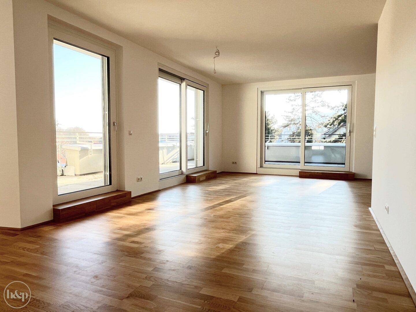 Lichtdurchfluteter Wohnbereich mit Holzboden und mehreren Fenstern, die Zugang nach draußen bieten.