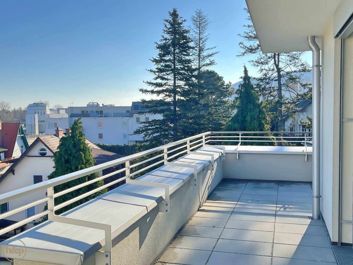 Große, geflieste Terrasse mit weißem Geländer und weitem Blick auf die Umgebung.