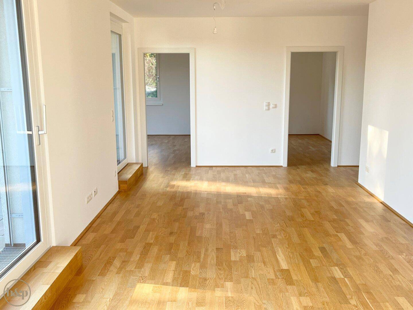 Geräumiges, helles Zimmer mit Holzboden und mehreren Türöffnungen zu weiteren Räumen.