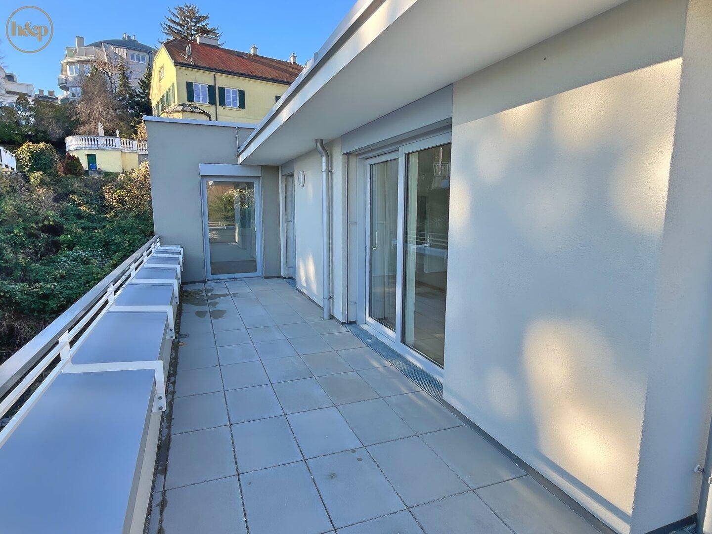 Lange Terrasse mit Fliesenboden und weißem Geländer, bietet Zugang zu mehreren Räumen.