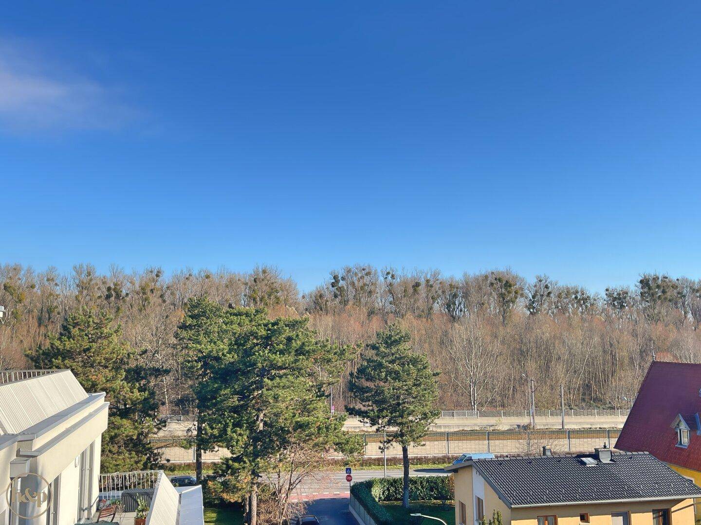 Weitläufiger Blick auf eine bewaldete Landschaft und eine Straße unter blauem Himmel.