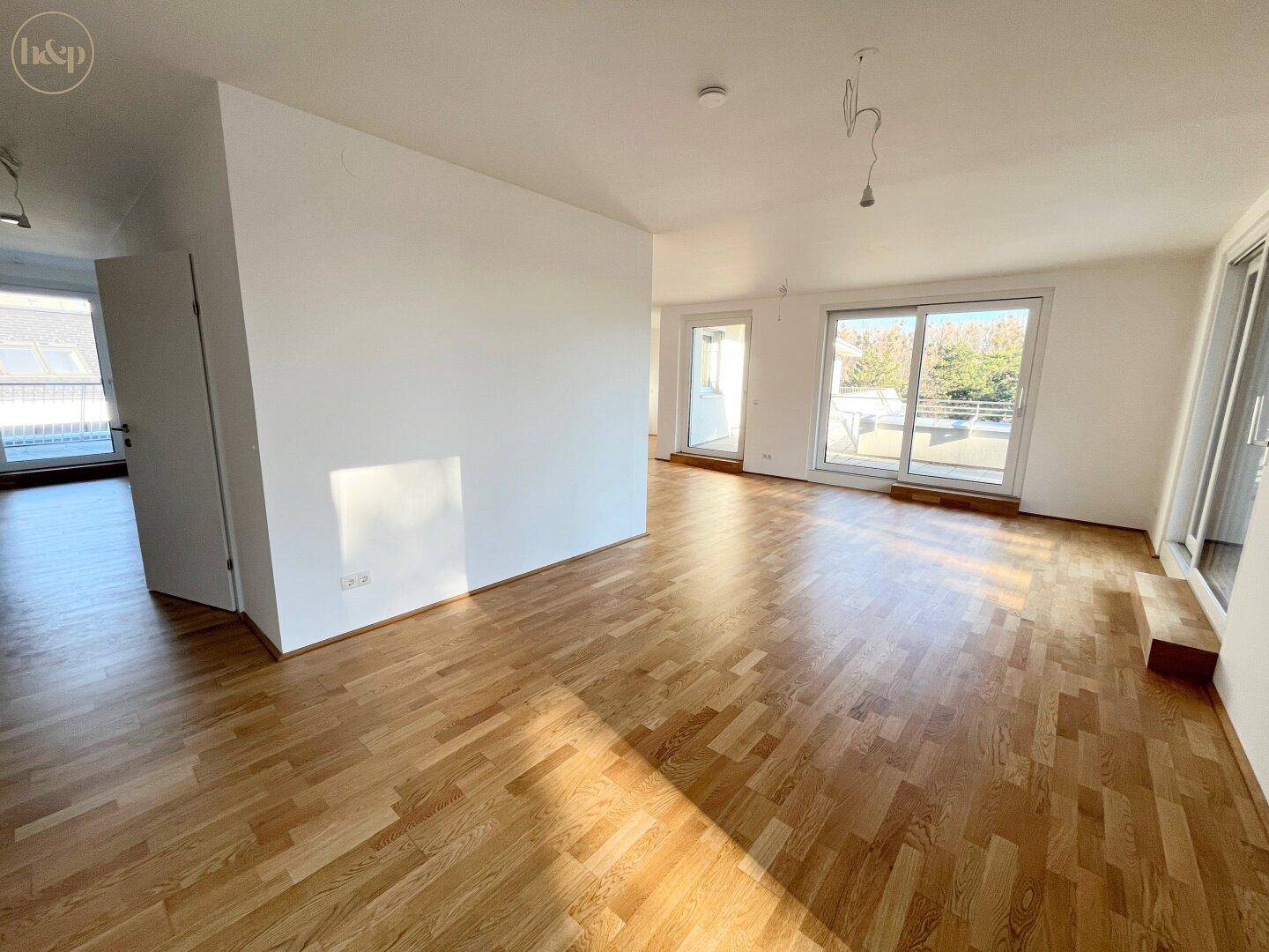 Offener, heller Wohnbereich mit Parkettboden und Zugang zu mehreren Außenbereichen.
