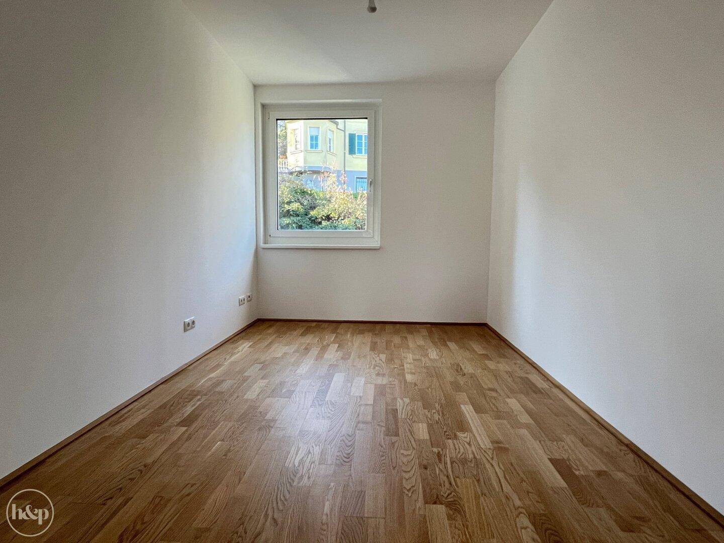 Geräumiges, helles Schlafzimmer mit Holzboden und einem Fenster mit Blick auf die Nachbarschaft.
