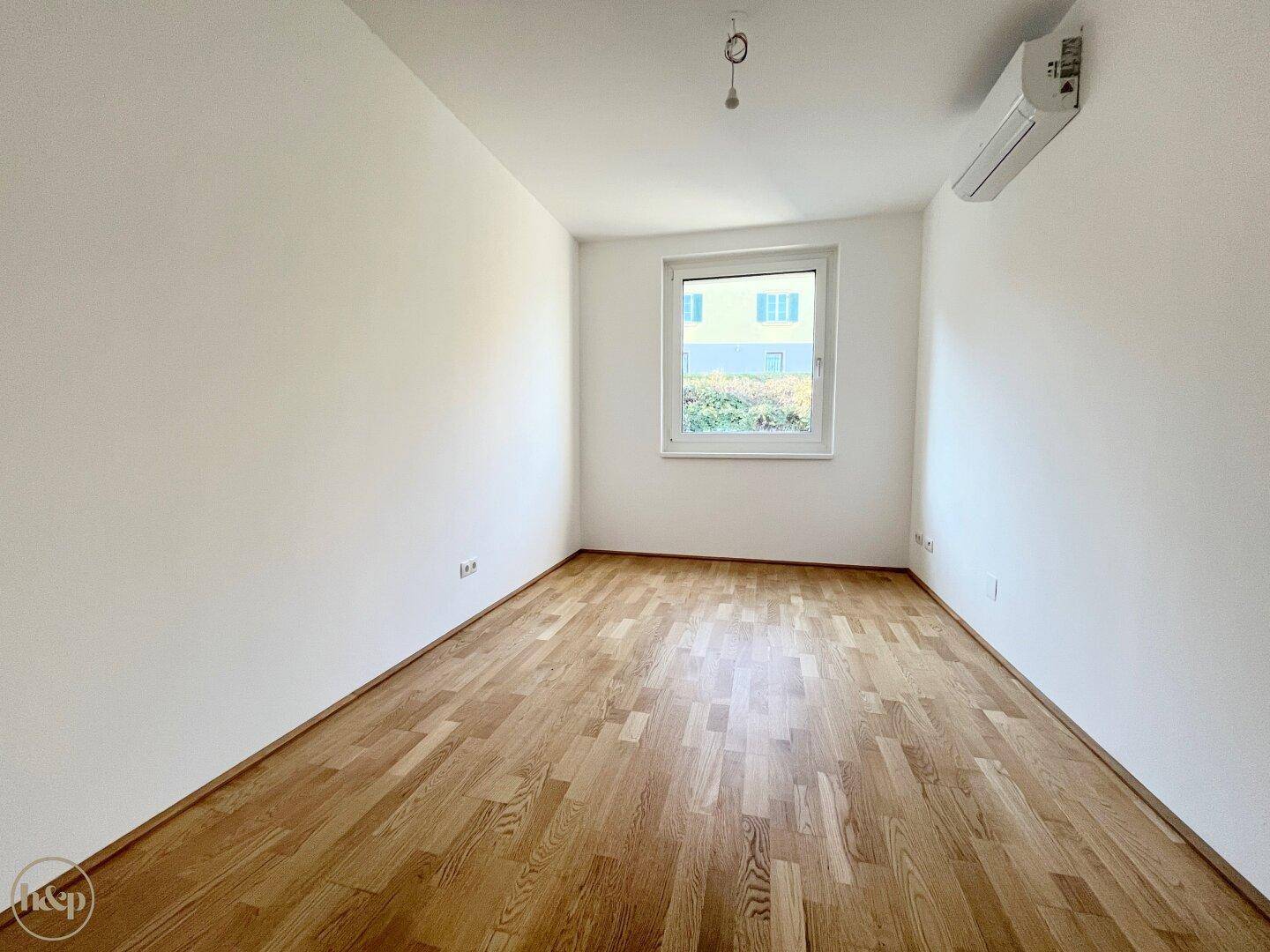 Helles Schlafzimmer mit Holzboden, Fenster und installierter Klimaanlage.