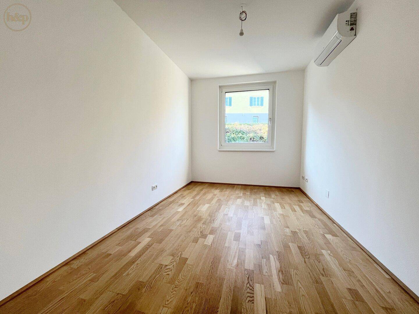 Helles Schlafzimmer mit Parkettboden, Fenster und installierter Klimaanlage.