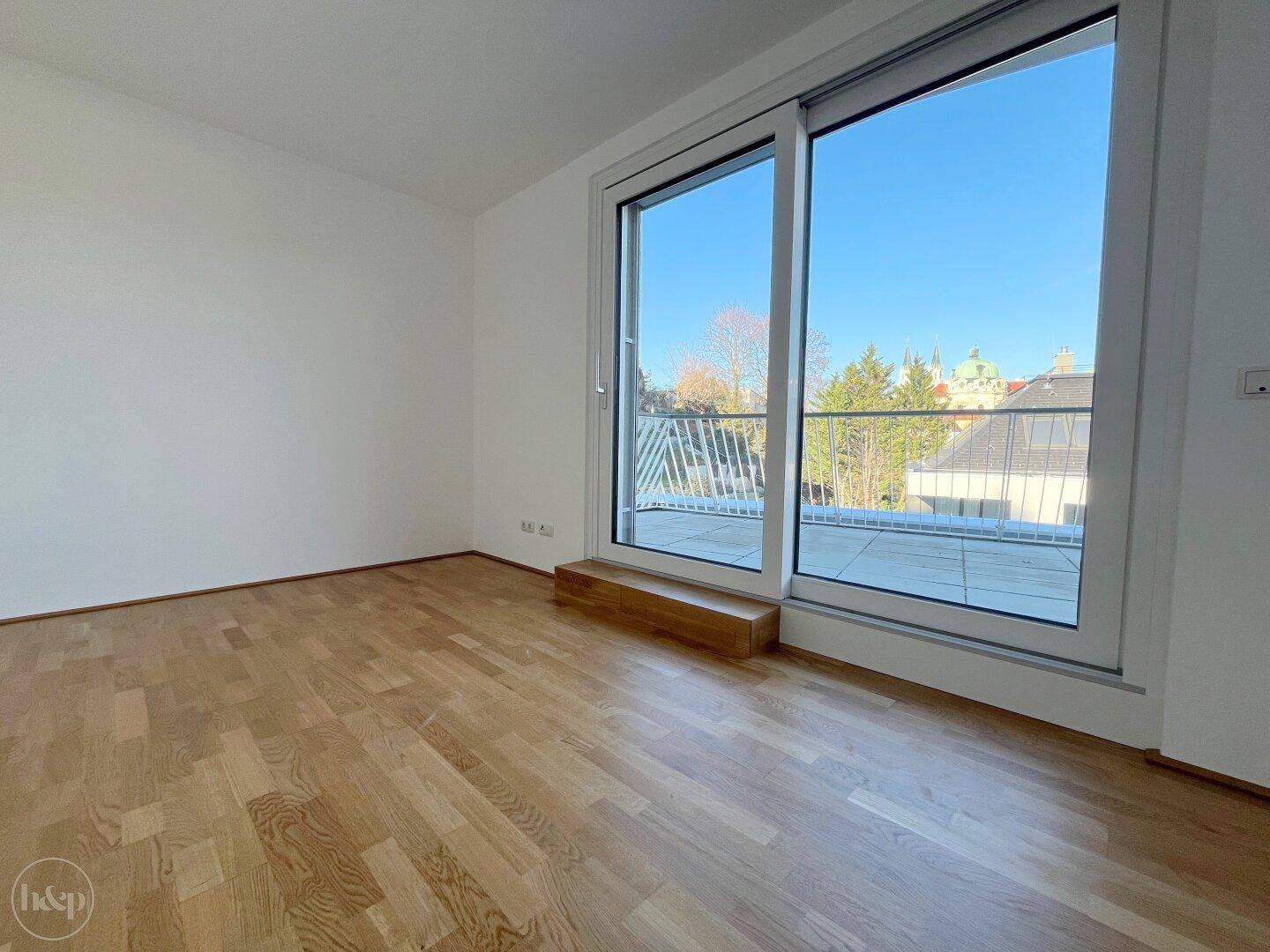 Heller Raum mit Holzboden und großer Schiebetür, die auf eine geflieste Terrasse führt.