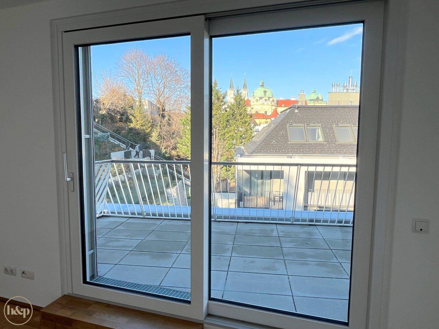 Geräumige Terrasse mit Fliesenboden und Blick auf die umliegenden Dächer und Bäume.