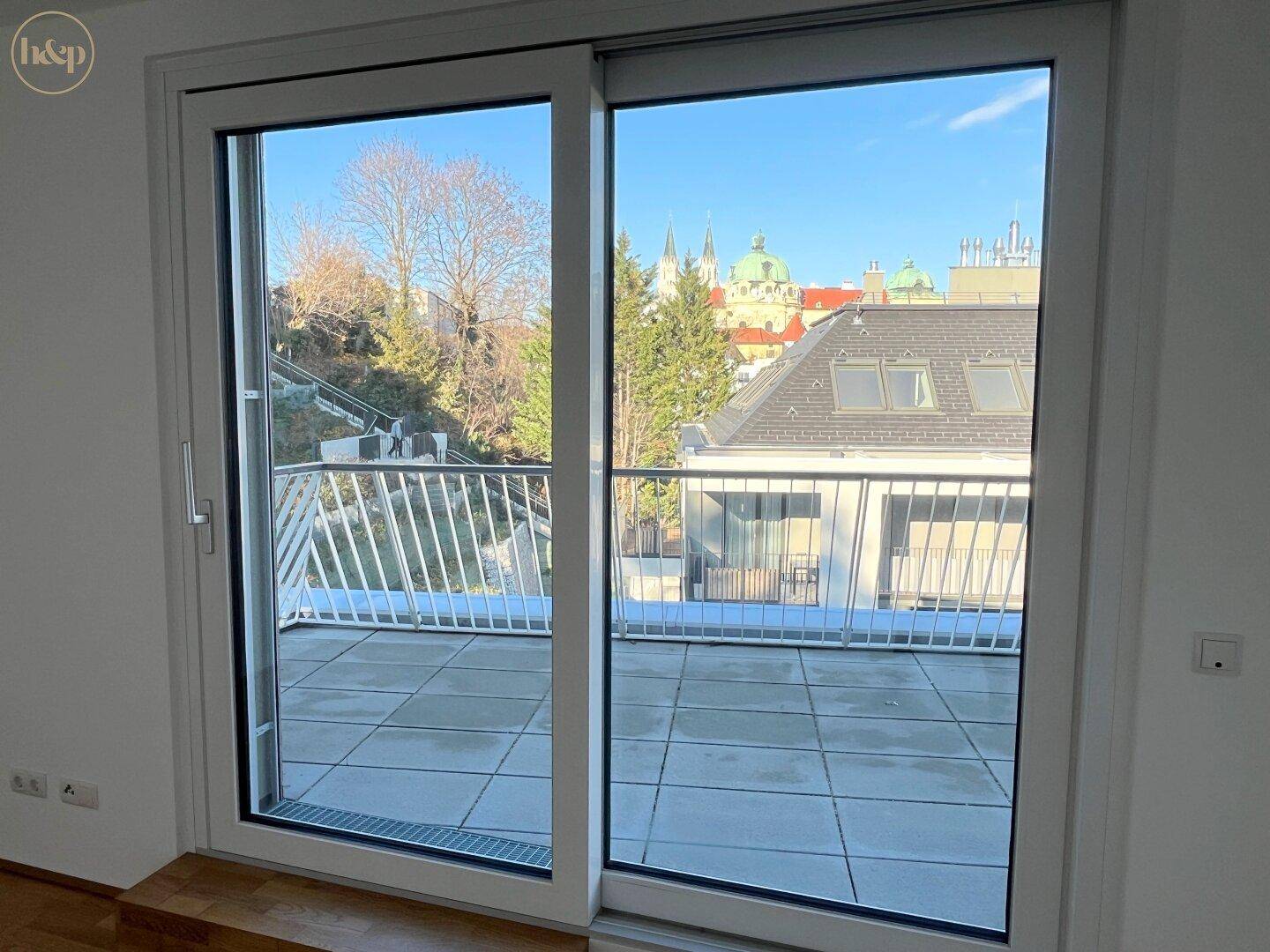 Große Glasschiebetür bietet Zugang zu einer gefliesten Terrasse mit Blick auf die Umgebung.