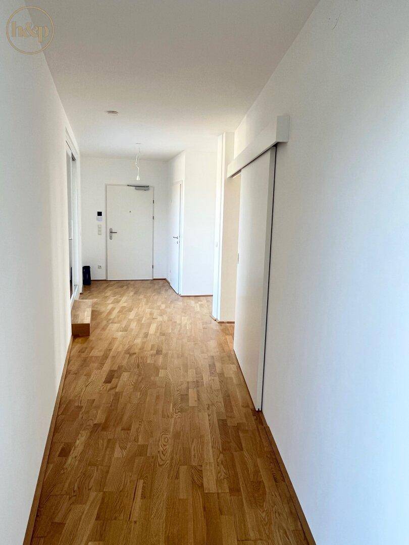 Eingangsbereich mit Holzboden und weiß gestrichenen Wänden, führt zu den Wohnräumen.