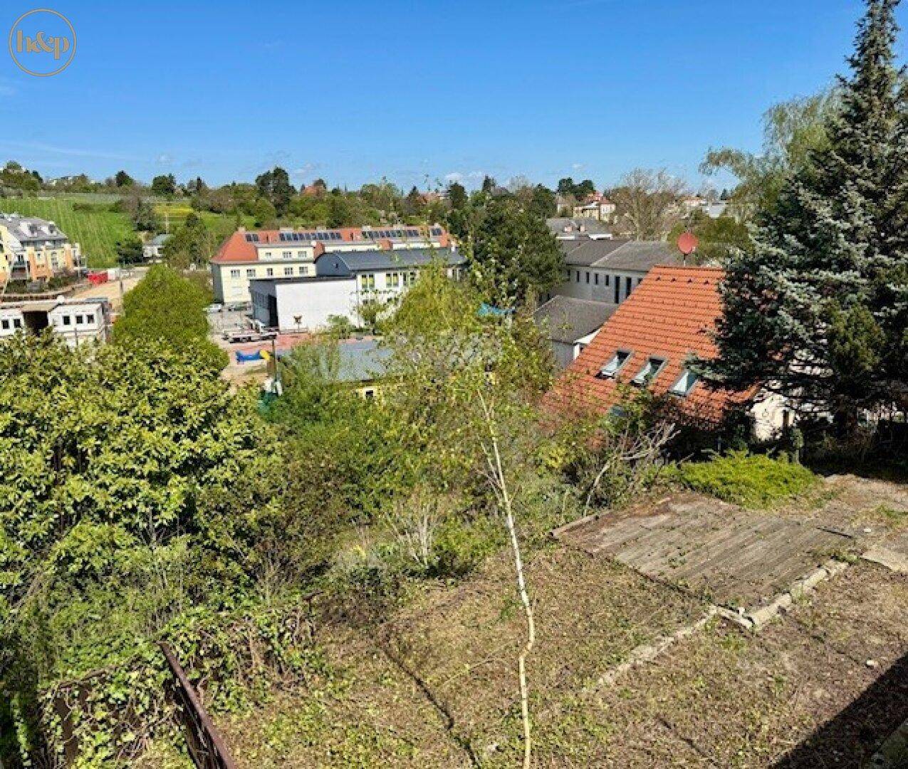 Weitläufiger Blick von oben auf einen Gartenbereich mit Bäumen und Wohngebäuden im Hintergrund.