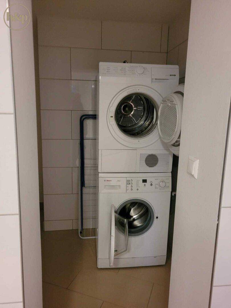 Praktischer Hauswirtschaftsraum mit gestapelter Waschmaschine und Trockner, umgeben von weißen Fliesen.