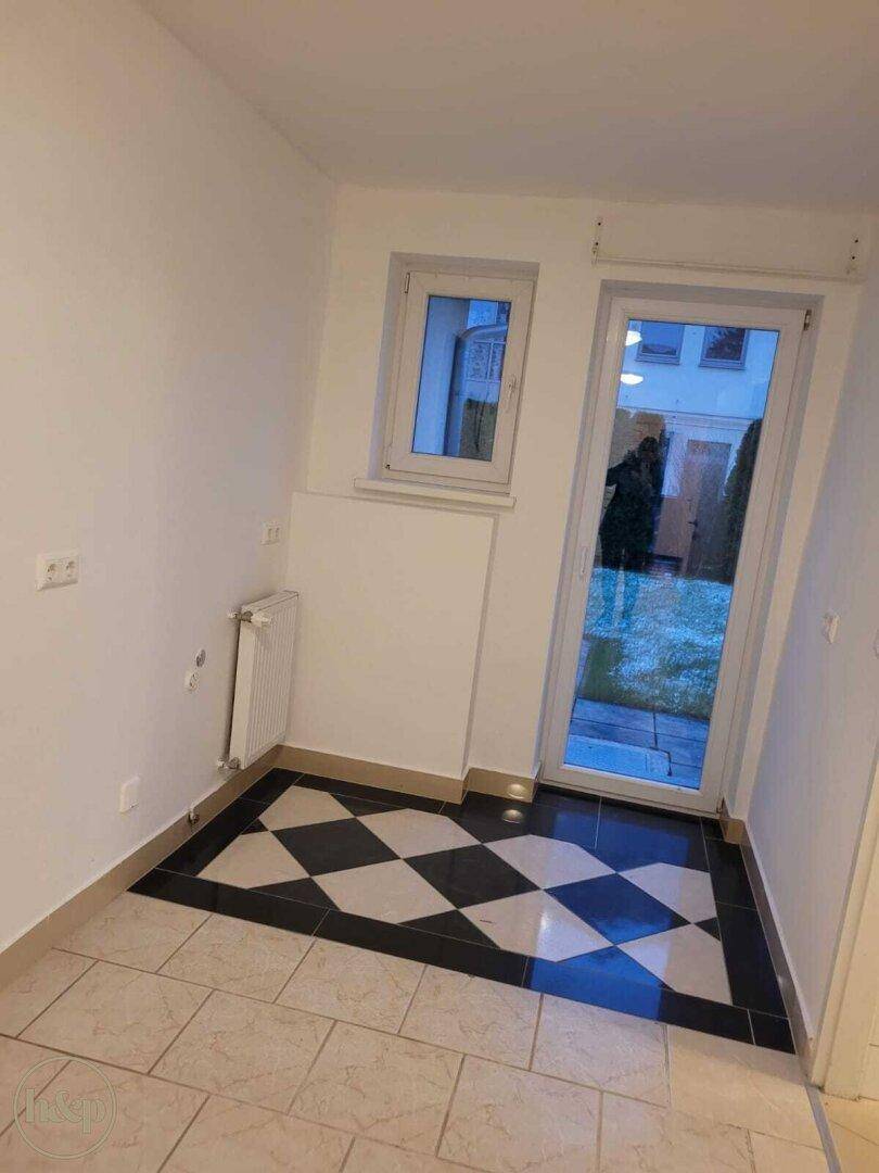 Heller Eingangsbereich mit schwarz-weiß gemusterten Fliesen und Zugang zum Garten.