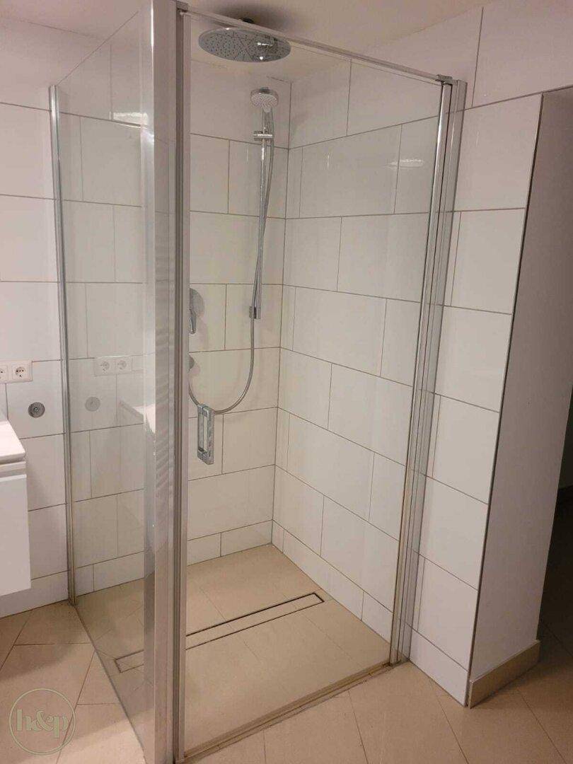 Modernes Badezimmer mit ebenerdiger Dusche, Glasabtrennung und weißen Fliesen.