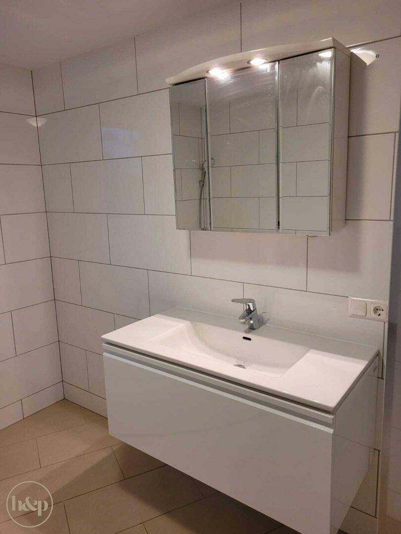 Badezimmer mit modernem Waschtisch, Spiegelschrank und weißen Wandfliesen.