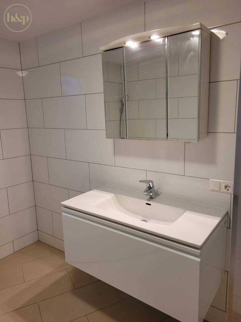 Modernes Badezimmer mit Einzelwaschbecken, Spiegelschrank und weißen Wandfliesen.