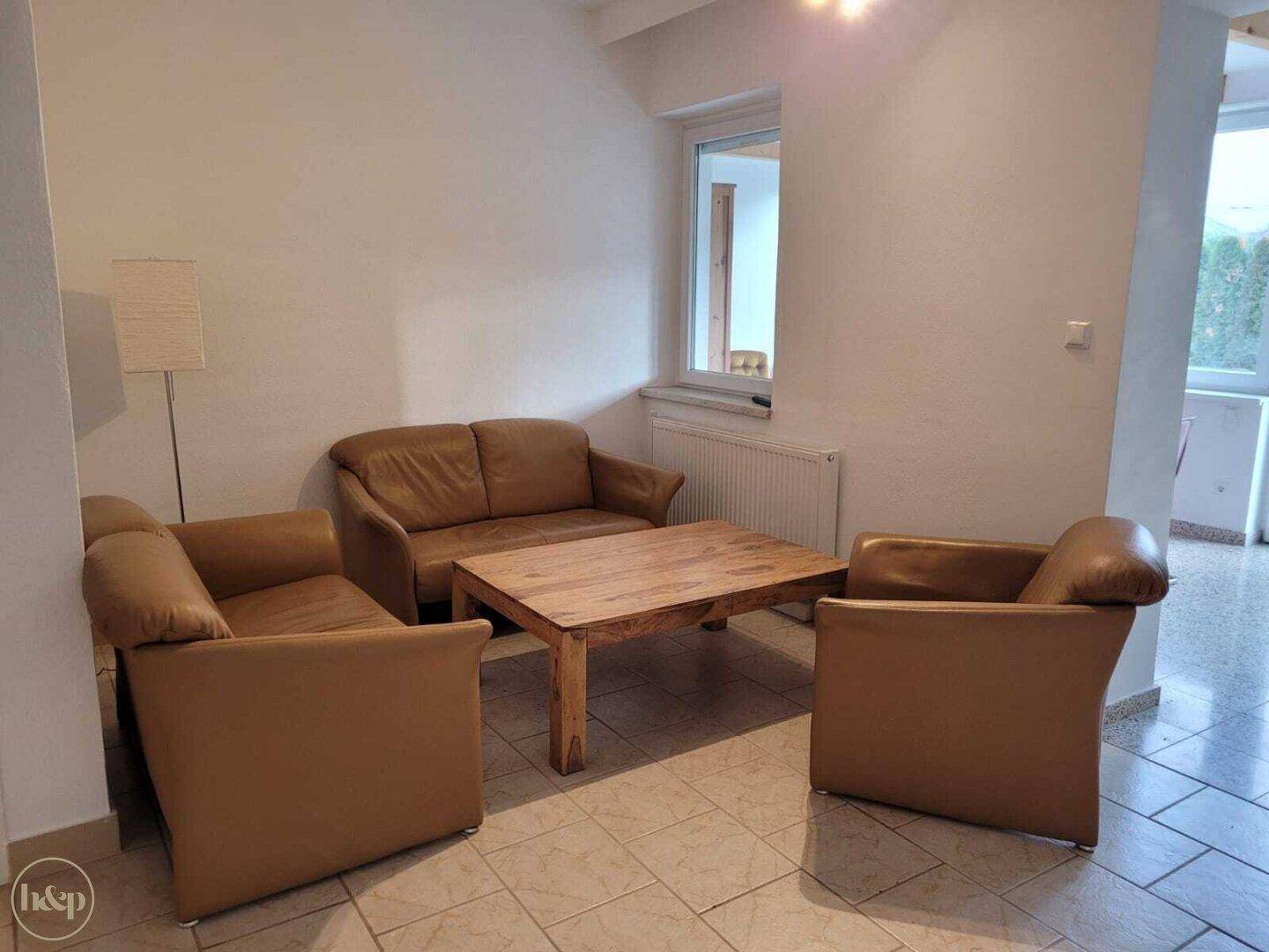 Gemütliches Wohnzimmer mit braunen Ledersofas, Holztisch und Fliesenboden.