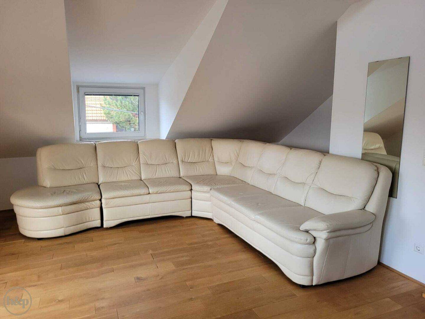 Geräumiges Wohnzimmer im Dachgeschoss mit großer beiger Ledercouch und Holzboden.
