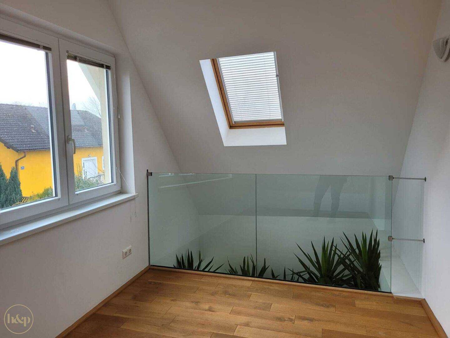 Heller Dachgeschossbereich mit Holzboden, Glasgeländer und Pflanzen als Dekoration.