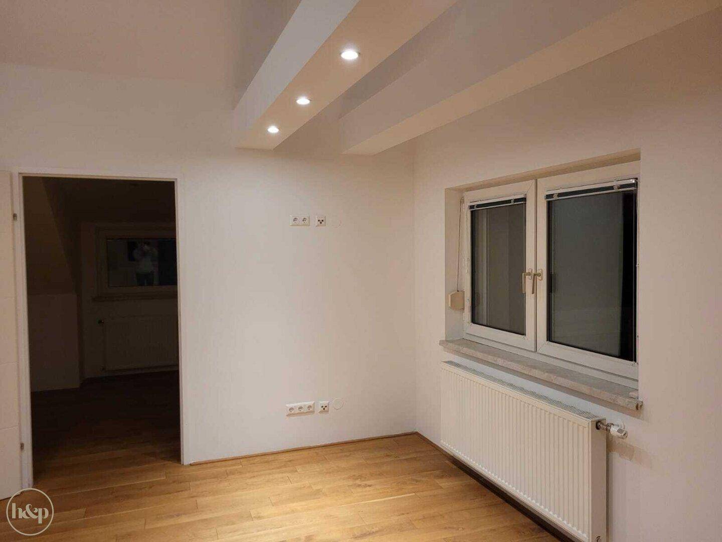 Helles Schlafzimmer mit Holzboden, Fenster und Einbaustrahlern in der Decke.