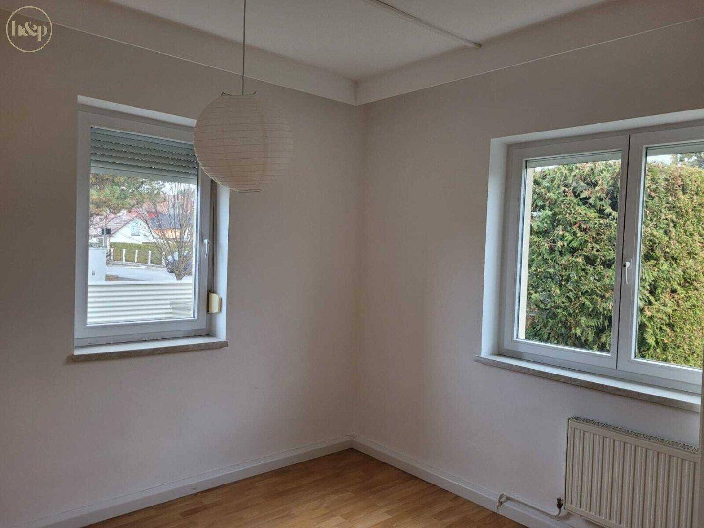 Helles Schlafzimmer mit Holzboden und zwei Fenstern, bietet viel natürliches Licht.