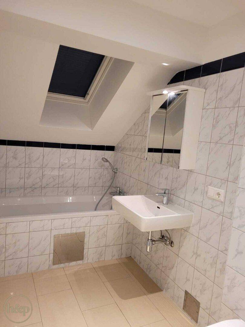 Badezimmer im Dachgeschoss mit Badewanne, Waschtisch und Dachfenster.