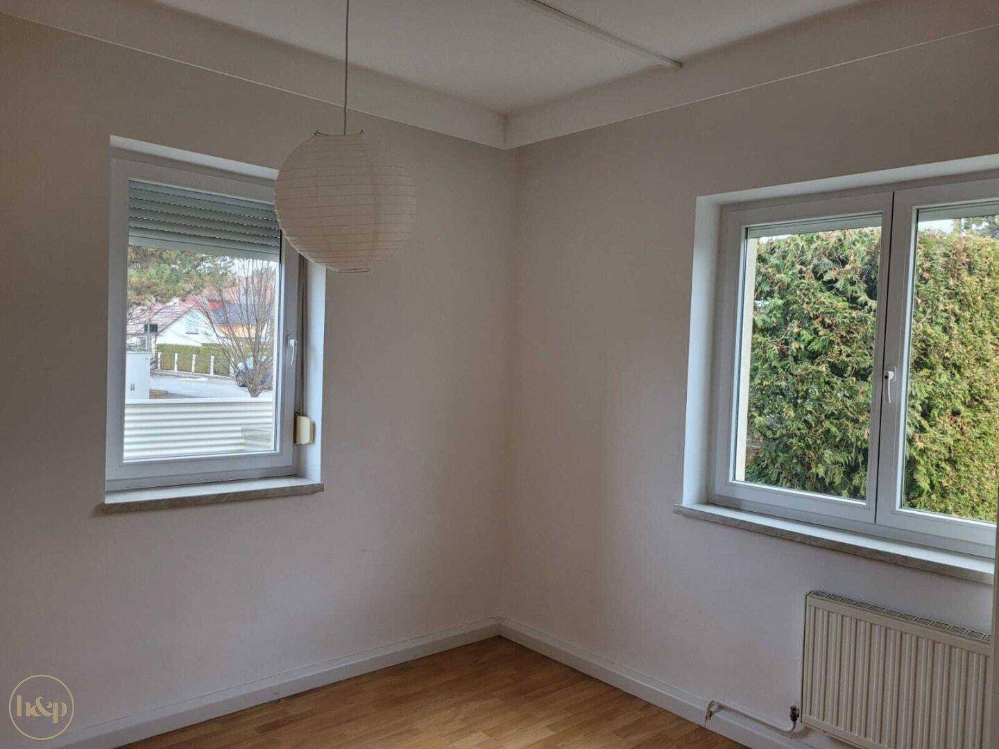 Helles Schlafzimmer mit Holzboden, zwei Fenstern und Blick ins Grüne.