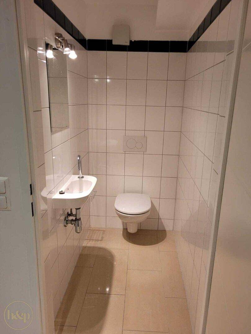 Kleines Gäste-WC mit wandhängender Toilette, Handwaschbecken und weißen Fliesen.