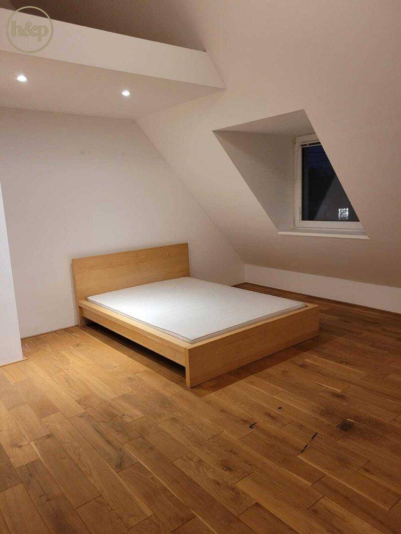 Schlafzimmer im Dachgeschoss mit Holzbettrahmen und schräger Decke auf Holzboden.