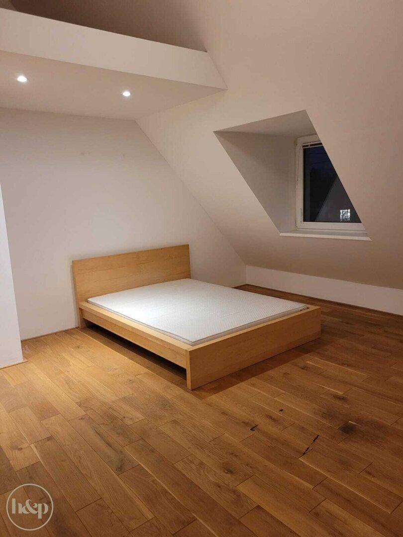 Schlafzimmer im Dachgeschoss mit Holzbettrahmen, Holzboden und Dachschräge.