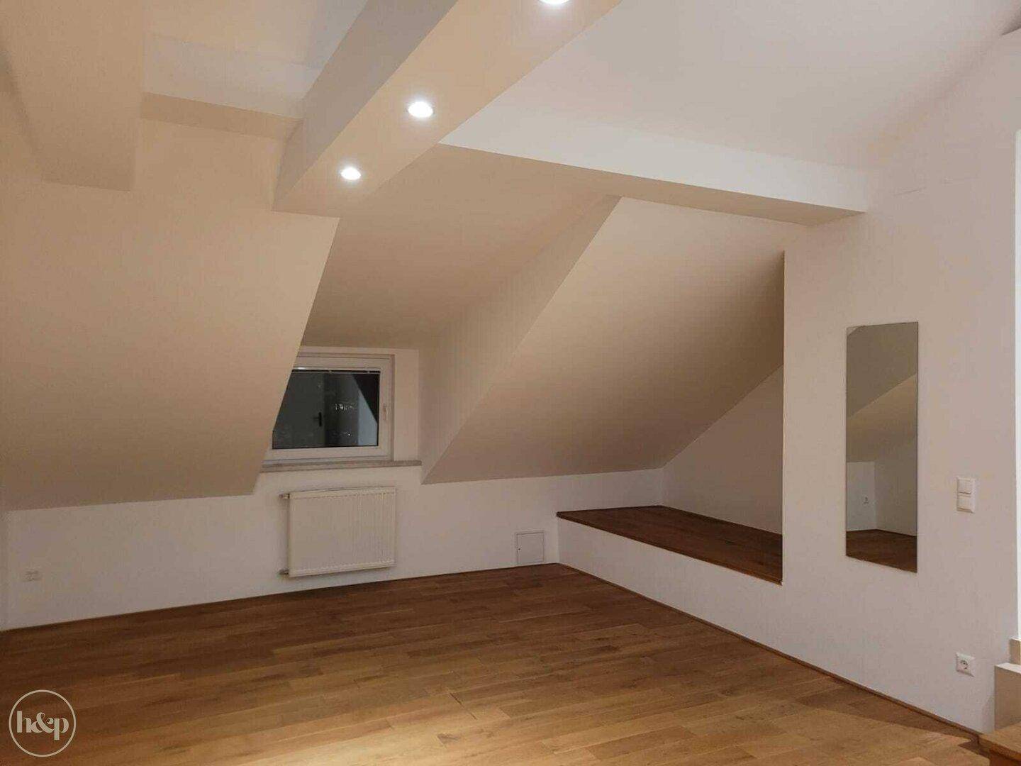 Geräumiges Wohnzimmer im Dachgeschoss mit Holzboden, Dachschräge und Einbaustrahlern.