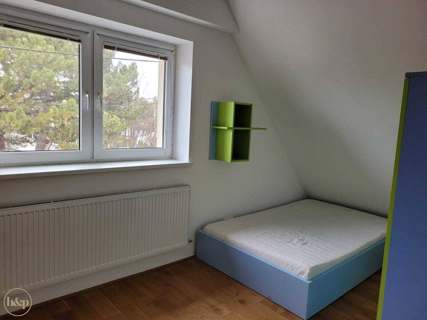 Kinderzimmer im Dachgeschoss mit blauem Bettrahmen, Holzboden und Fenster.