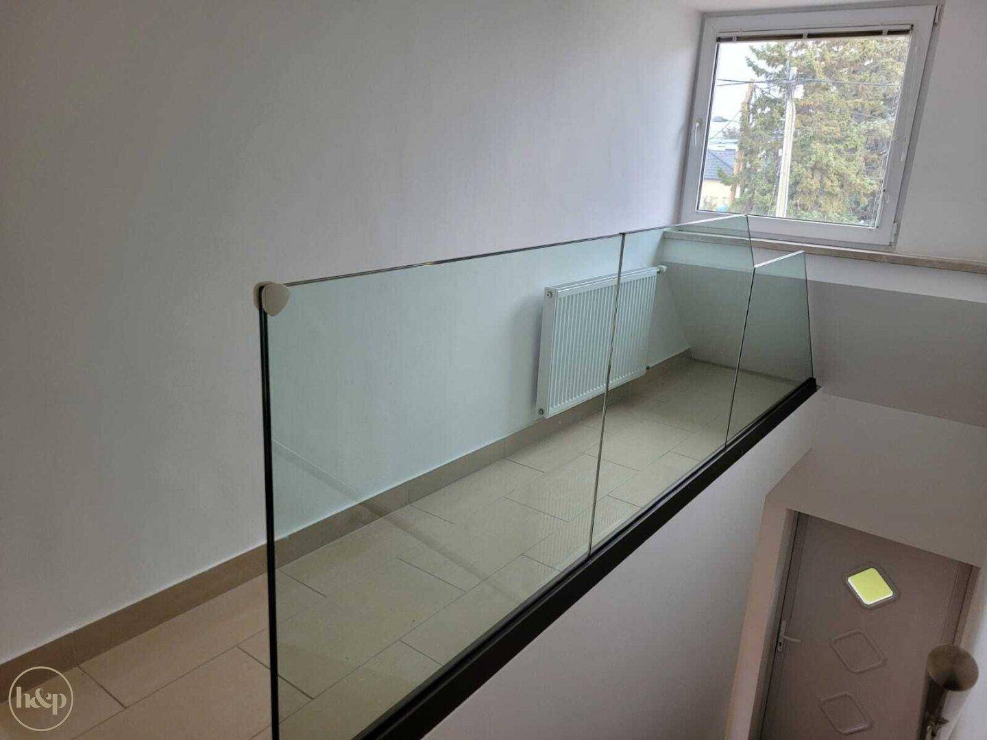 Heller Flur mit moderner Glasbrüstung, weiß gestrichenen Wänden und einem Fenster.