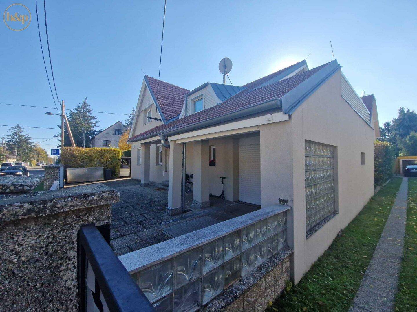 Seitenansicht des Hauses mit gepflastertem Bereich, Garagenzufahrt und dekorativer Glasbausteinwand.