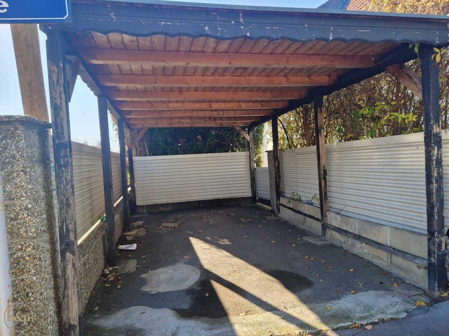 Überdachter Carport mit Holzbalken und Wellblechwänden neben der Straße.