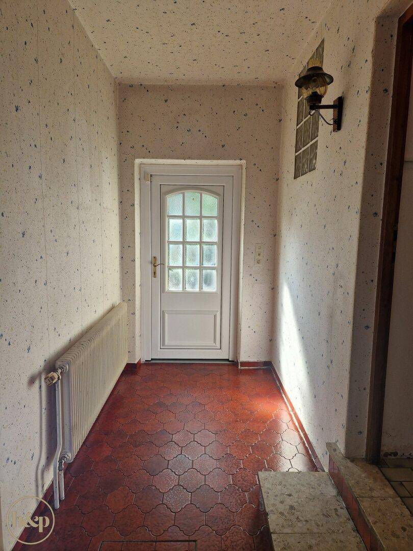 Langer Flur mit gemusterten Tapeten, Fliesenboden und einer Eingangstür.